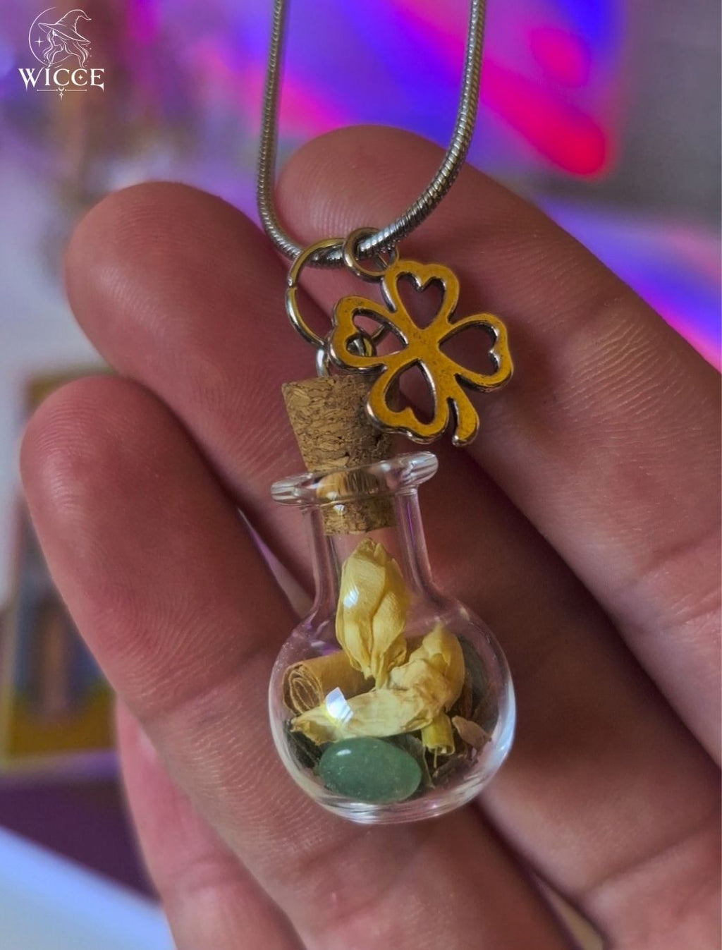 Good Luck talisman necklace with a four-leaf clover charm, glass vial filled with herbs, flowers and a green aventurine held by hand.