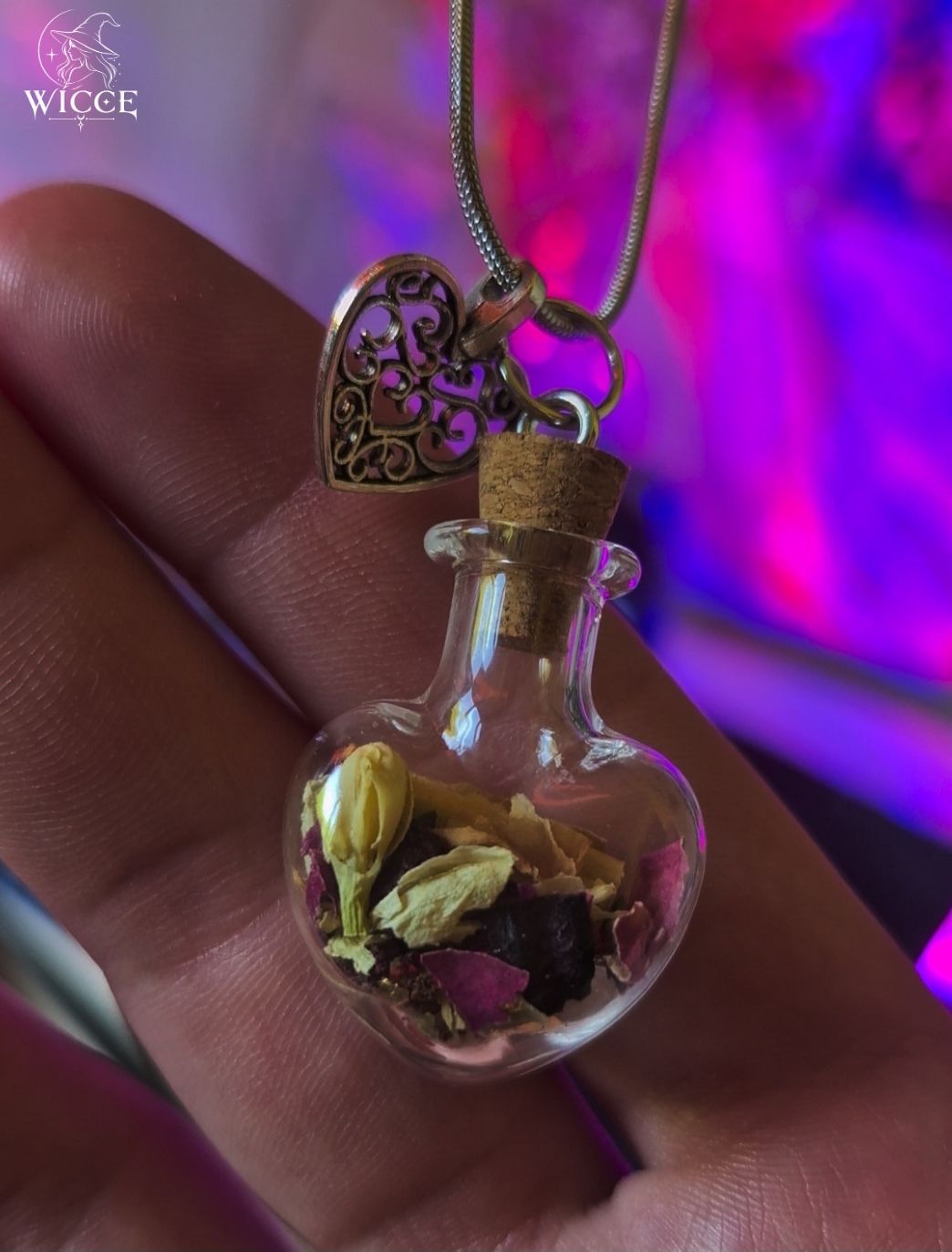 Love talisman necklace with jasmine, rose petals, and heart charm held by hand.