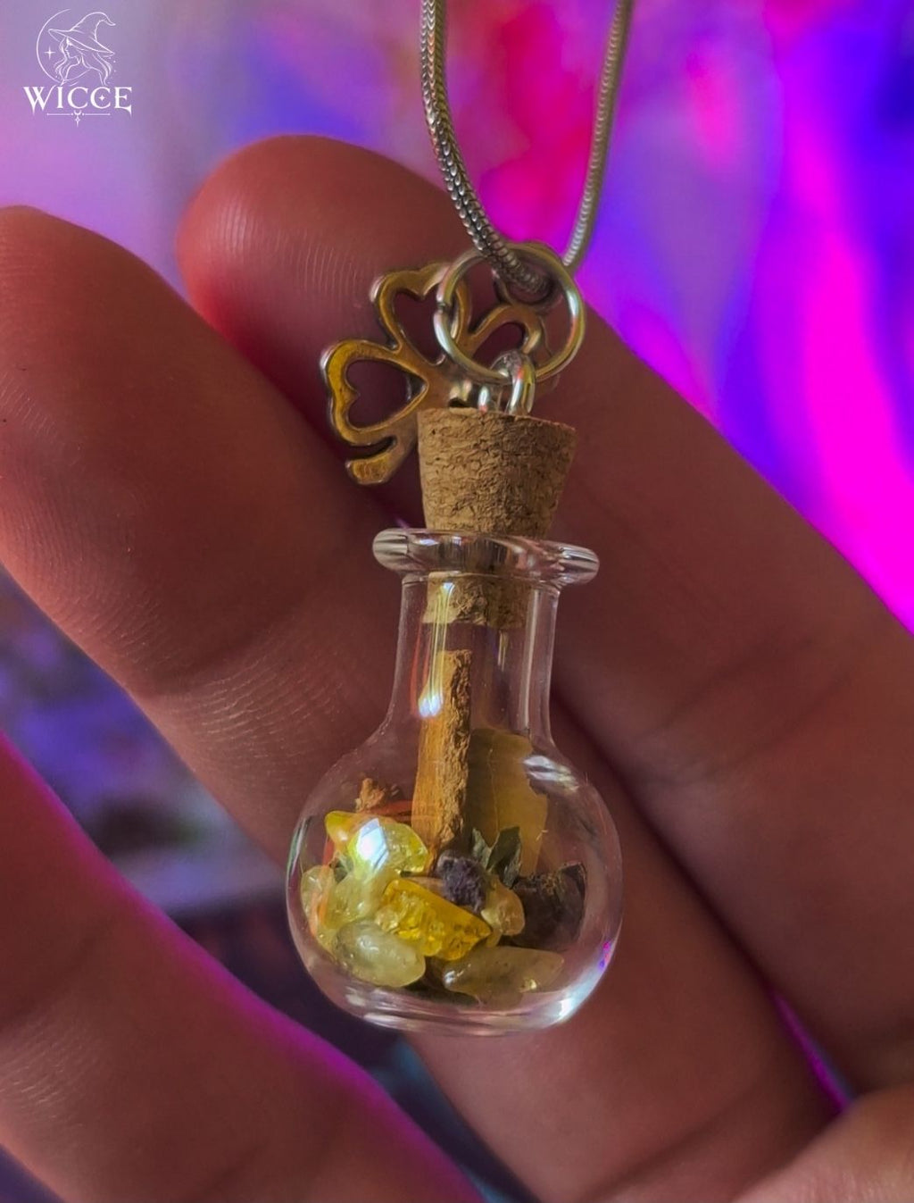 Money Magnet talisman necklace with a clover charm, glass vial filled with cinnamon, citrine and herbs held by hand.